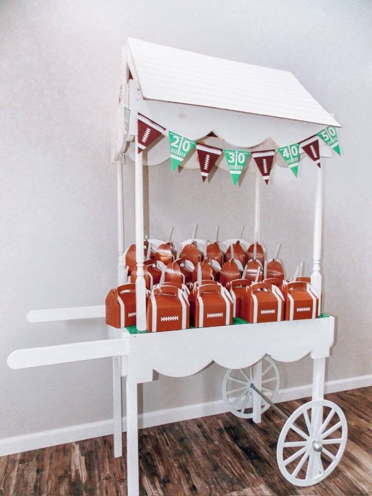 White wooden candy cart with a yard line pennant banner filled with football favor boxes