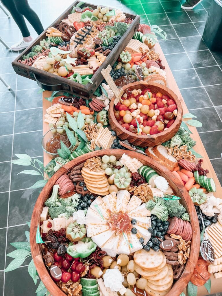 Long grazing table with meats, cheese, crackers, fruit and veggies in wooden bowls for a football party