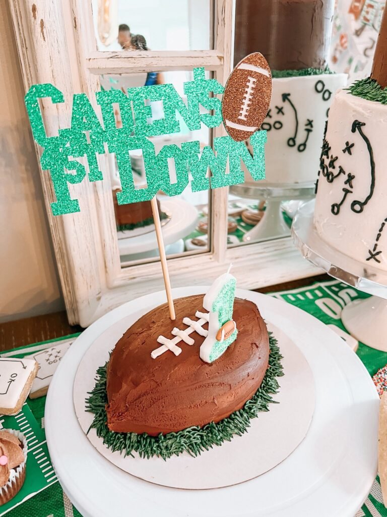 Chocolate football shaped smash cake on green piped grass with a glitter 1st Down topper