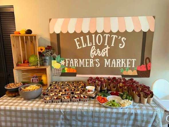 Farmers market food table with a striped awning banner, wooden crates of produce and a gingham tablecloth