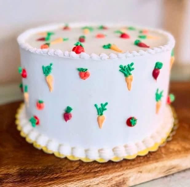 White 1st birthday cake with tiny piped carrots and tomatoes and a yellow piped border