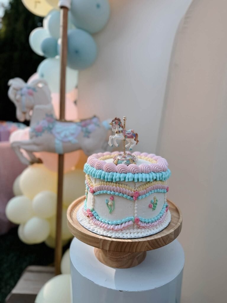 Pastel carousel birthday cake with a horse topper in front of balloons
