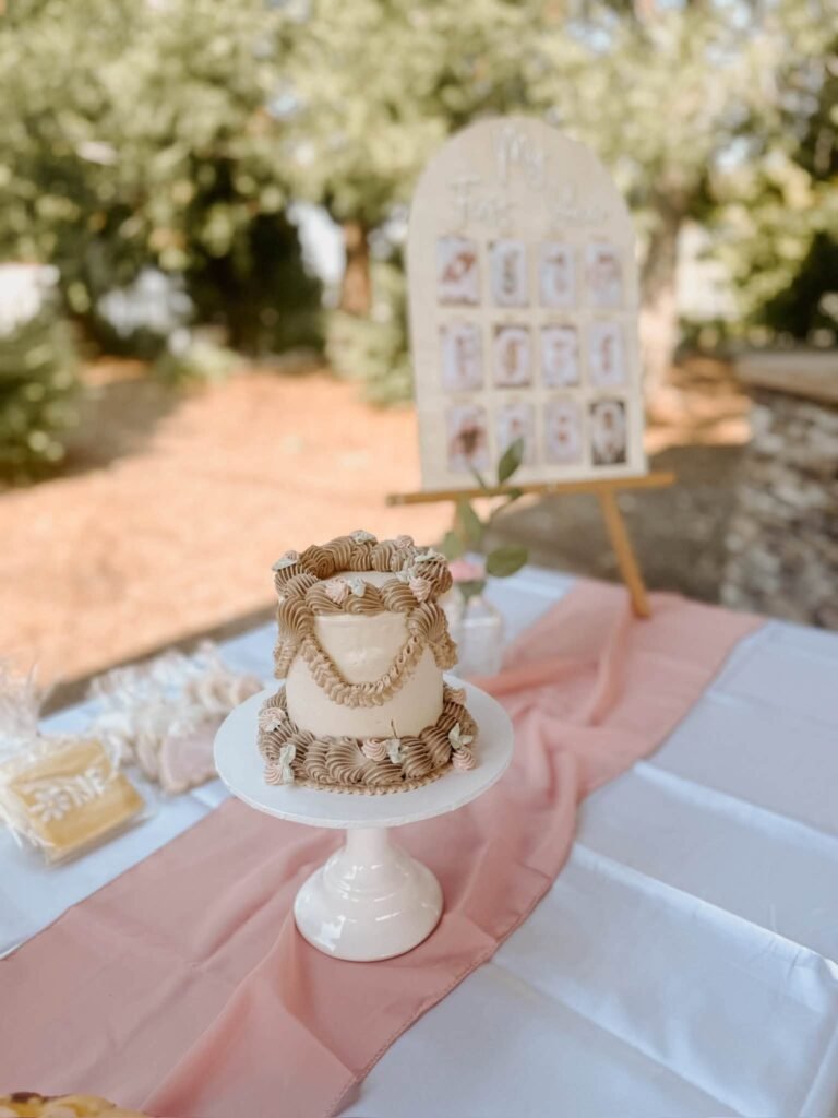 Birthday cake on a white pedestal stand on a pink table runner with a welcome sign