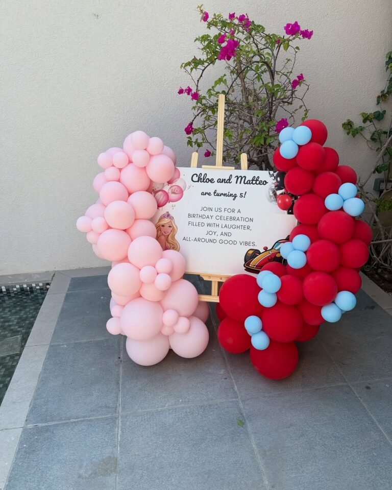 Birthday welcome sign on an easel framed with pink balloons on one side and red and blue balloons on the other