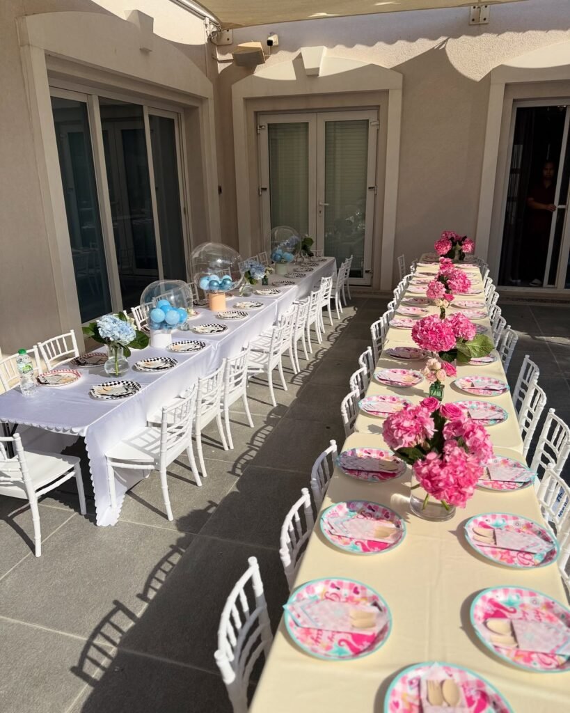 Two long outdoor party tables, one pink with pink hydrangeas and one white with race car plates and blue balloon centerpieces