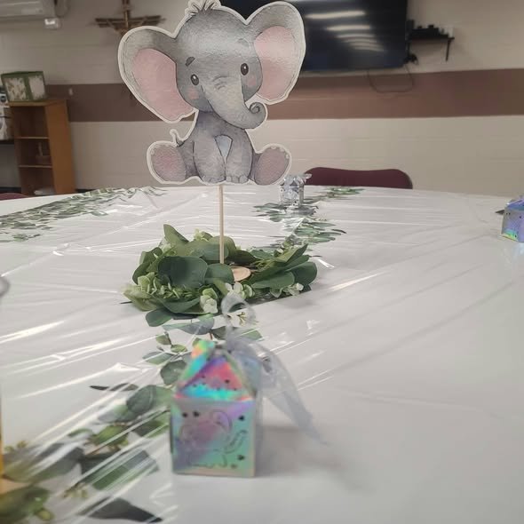 Gray elephant centerpiece on a stick in a holographic box with a greenery wreath on a white table