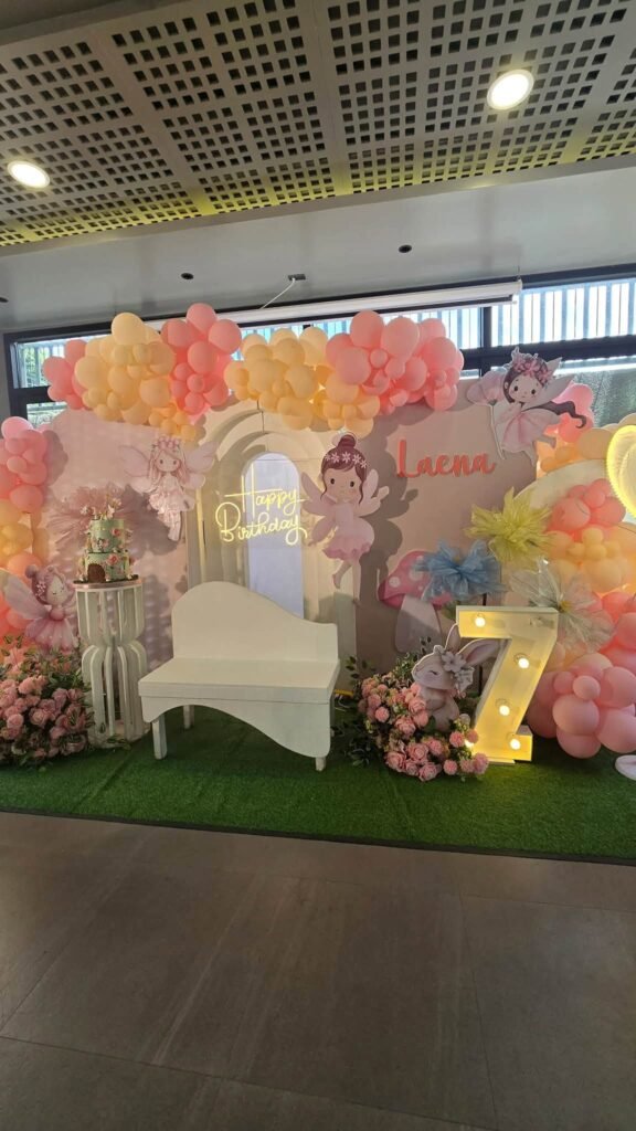 Fairy 7th birthday backdrop with pastel balloons, fairy cutouts, a white bench and a light up number 7
