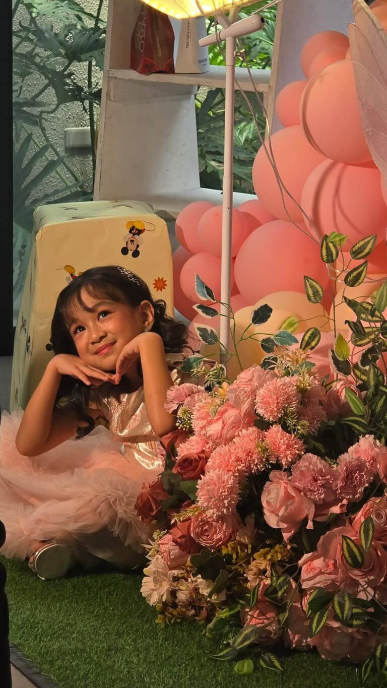 Birthday girl in a pink tulle dress posing by pink flowers and peach balloons at a fairy party