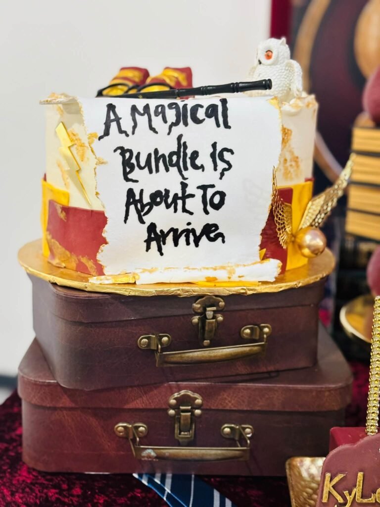 Harry Potter baby shower cake that says A Magical Bundle Is About to Arrive on stacked vintage suitcases with gold snitch wings and an owl