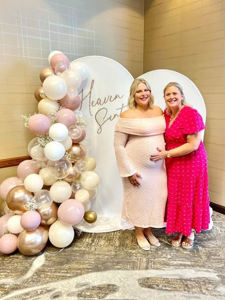Mom to be and guest by a Heaven Sent arch backdrop with blush and gold balloons