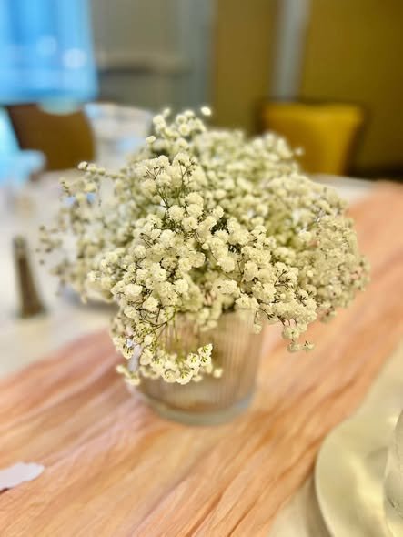 Baby breath flowers in a silver vase on a pink cheesecloth table runner