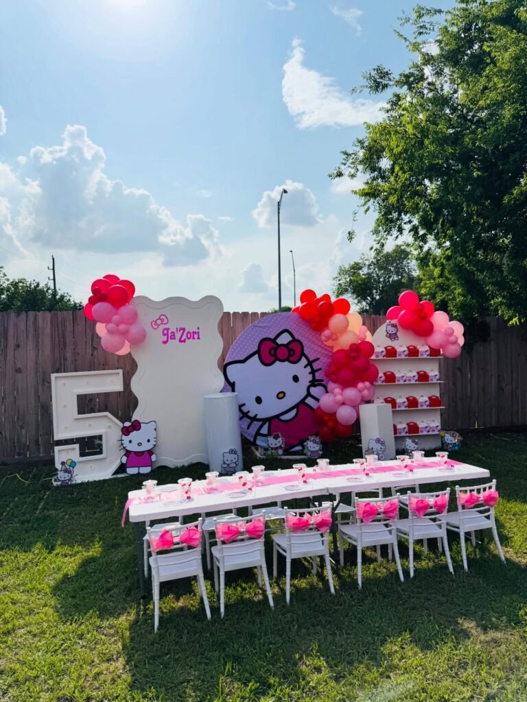 Backyard Hello Kitty birthday setup with a marquee number 5, round and wavy backdrop panels, balloons and long kids tables