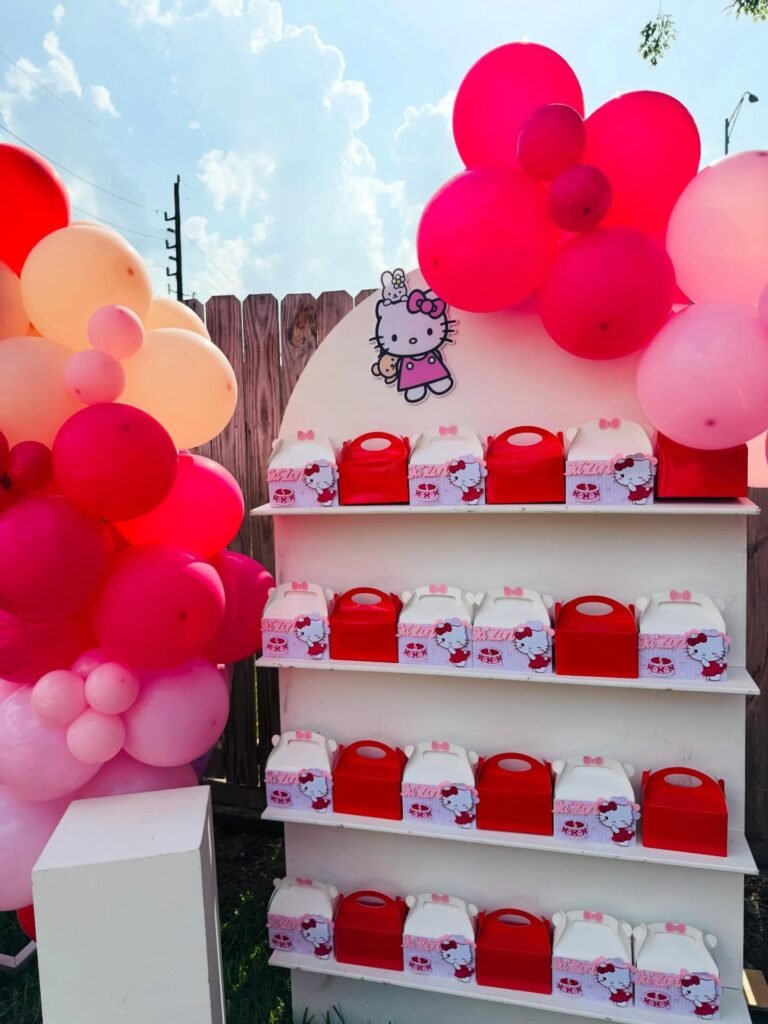 White shelf filled with red Hello Kitty treat boxes next to a pink and red balloon garland
