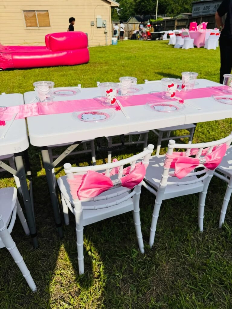 White kids chairs with pink bows tied on the back at a backyard Hello Kitty party table