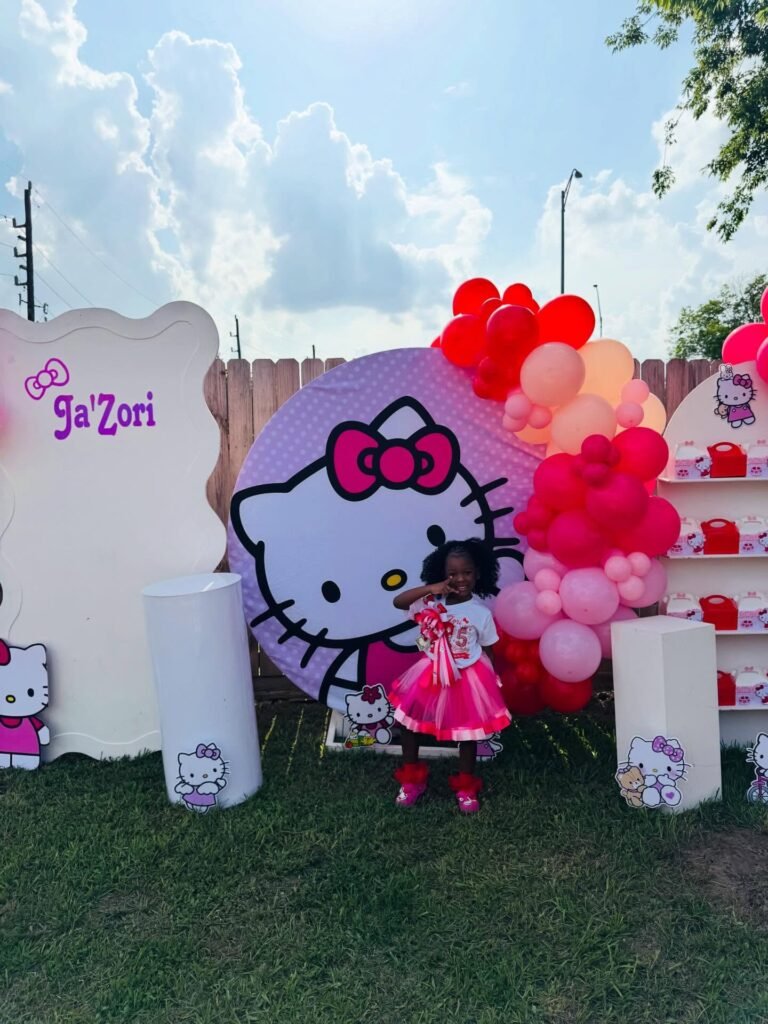 Birthday girl in a pink dress in front of a Hello Kitty backdrop with balloons