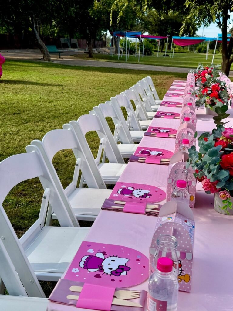 Row of white folding chairs along a pink Hello Kitty table in a park