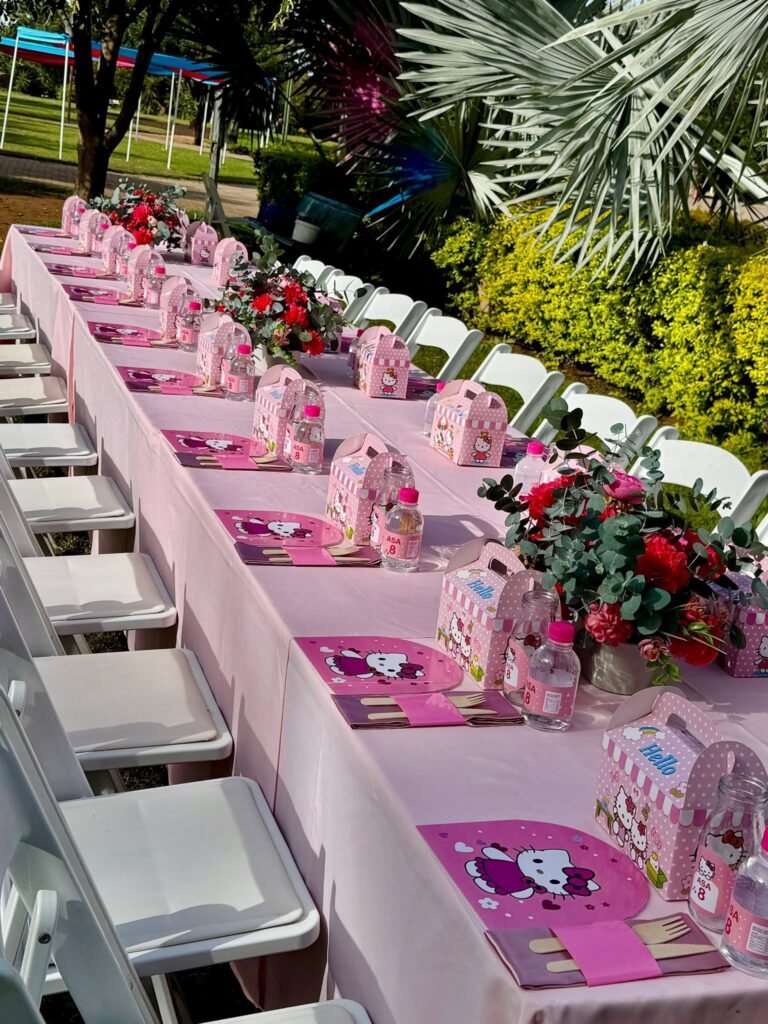 Red rose and greenery centerpieces down a long pink table with Hello Kitty treat boxes