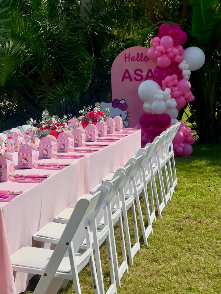 Hello Kitty name sign with a pink and red balloon garland at the end of a long table