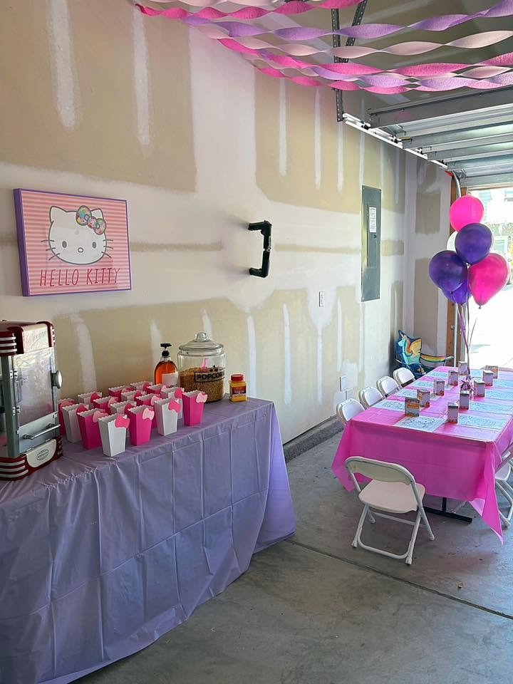 Garage Hello Kitty party with pink and purple streamers on the ceiling, a popcorn table and a long kids table