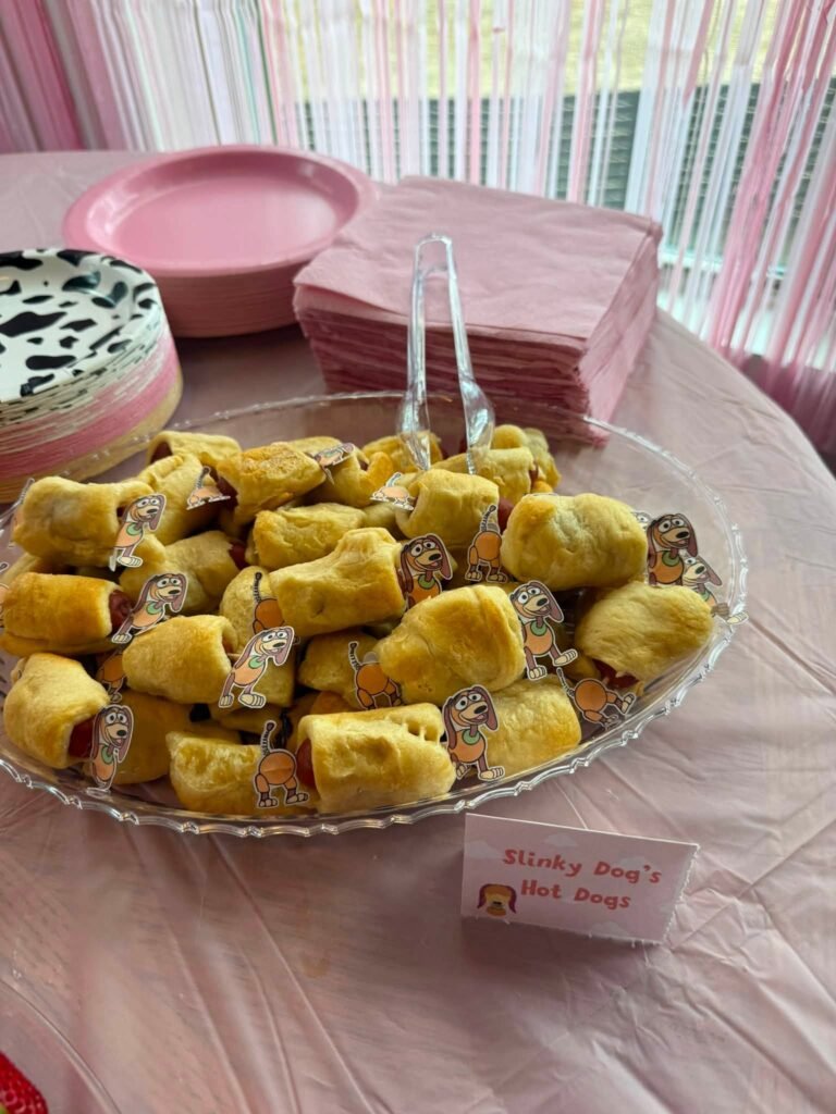 Slinky Dog hot dogs, mini pigs in a blanket on a pink tablecloth with cow print plates