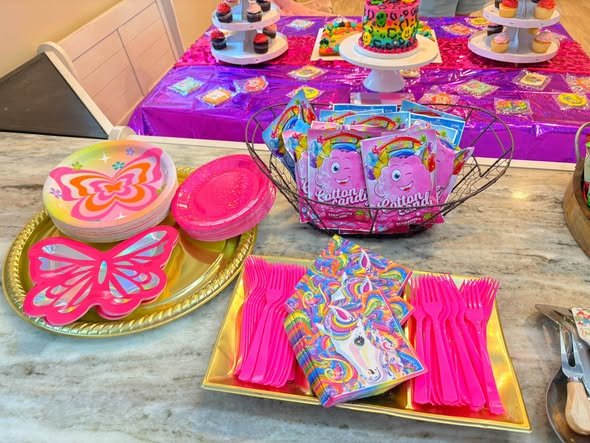 Lisa Frank party supplies with bright plates, butterfly plates, pink forks and themed napkins on a counter