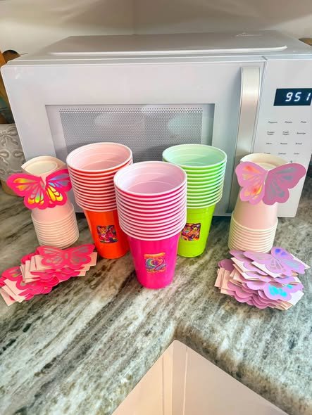 Stacks of neon pink, orange, green and pink cups with butterfly plates and napkins