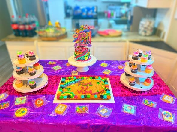 Lisa Frank dessert table with a rainbow sheet cake, cupcake stands and a purple tablecloth