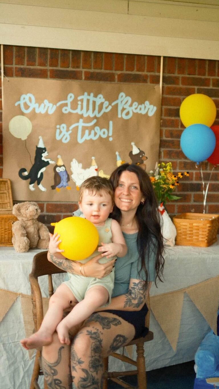 Mom holding the birthday boy in a sage romper at the Little Bear party table
