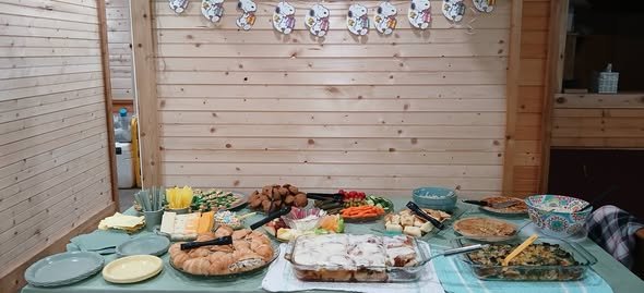 Baby shower food table with trays of pasta, salads, fruit and snacks on sage plates
