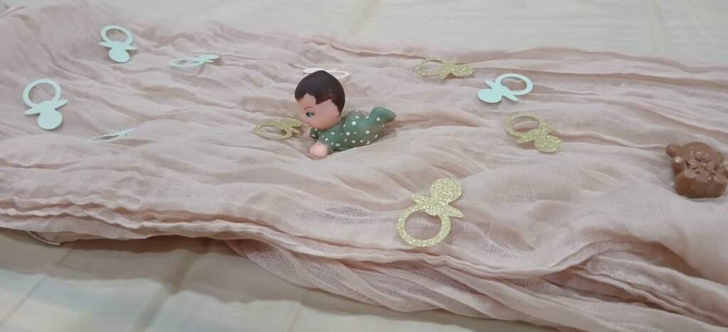 Pink cheesecloth table runner with pacifier confetti and a small baby figure