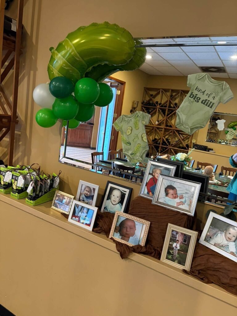 Green pickle balloon over a table with framed baby photos and a onesie