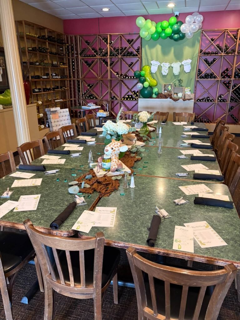 Long baby shower table in a wine cellar room with green balloons and white place cards
