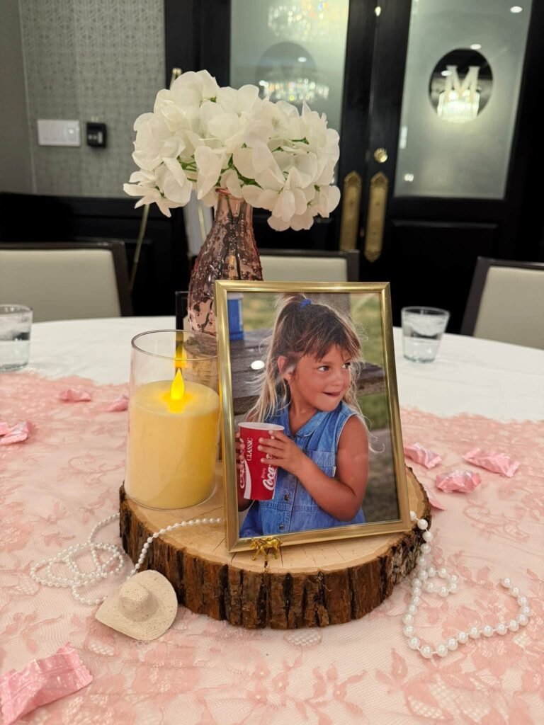 Centerpiece with a framed child photo, white flowers and a candle on a wood slice