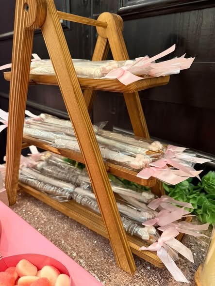 Wooden A frame stand holding chocolate dipped pretzel rods wrapped in clear bags with pink bows