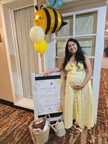 Mom to be in a yellow button front dress next to a bee balloon