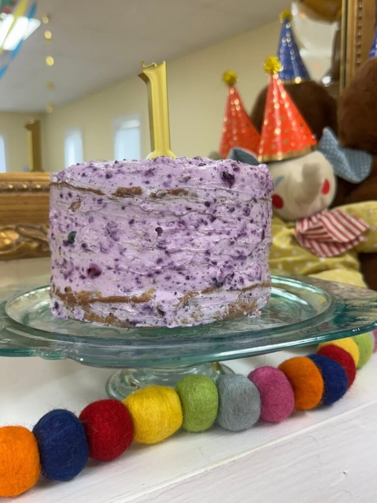 Purple blueberry smash cake with a gold number 1 and plush animals in party hats