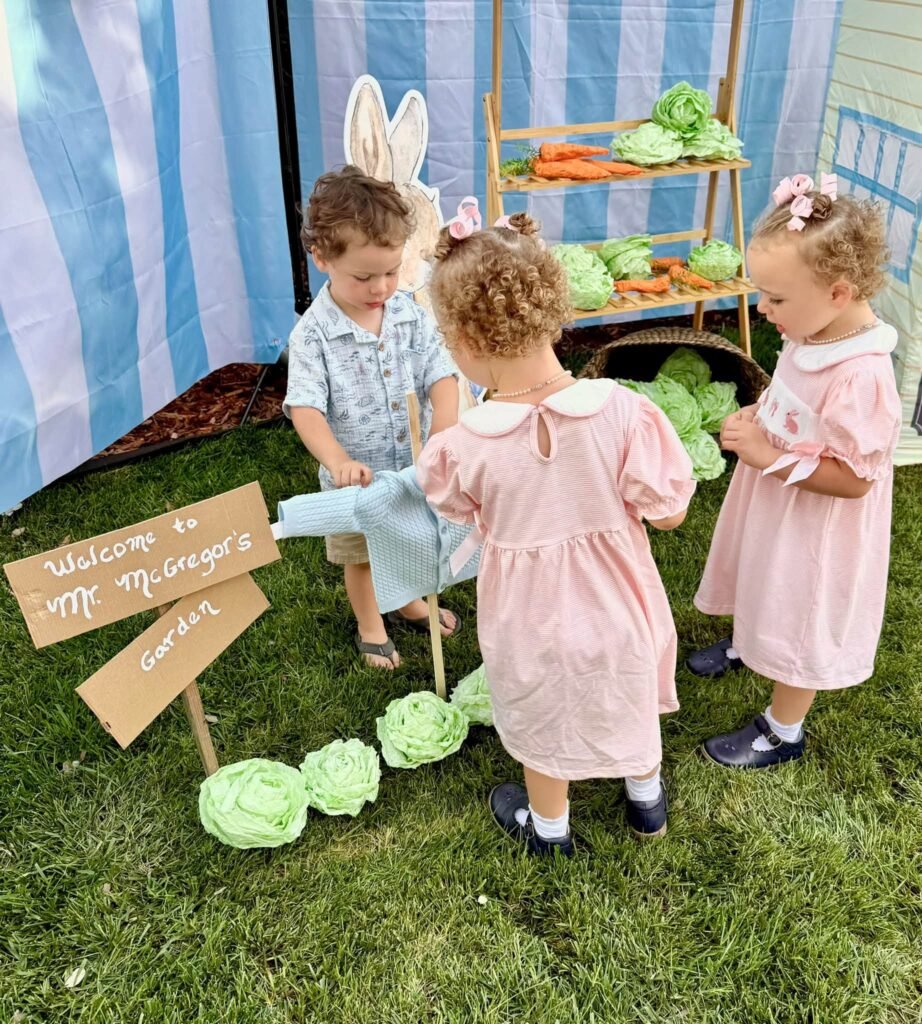 Toddlers in bunny ears and smocked outfits by a Welcome to Mr McGregor garden sign