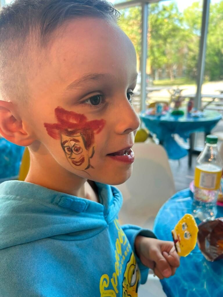 Boy with character face paint holding a SpongeBob lollipop at a birthday party