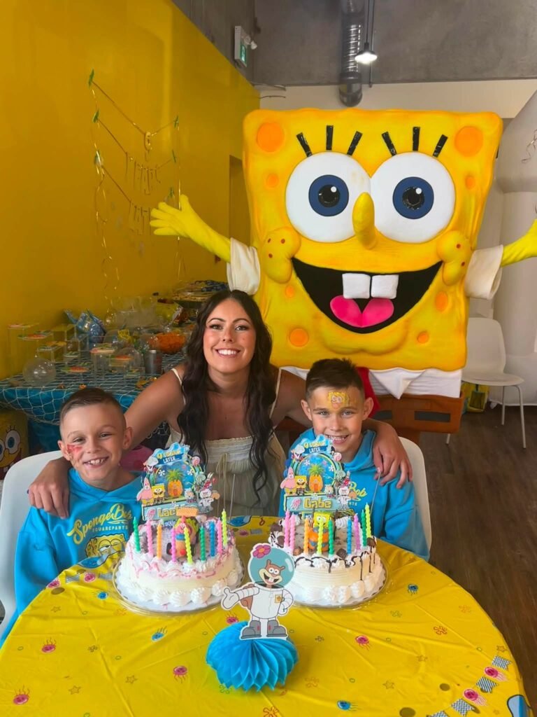 SpongeBob mascot with two birthday boys and their SpongeBob cakes at a yellow party table