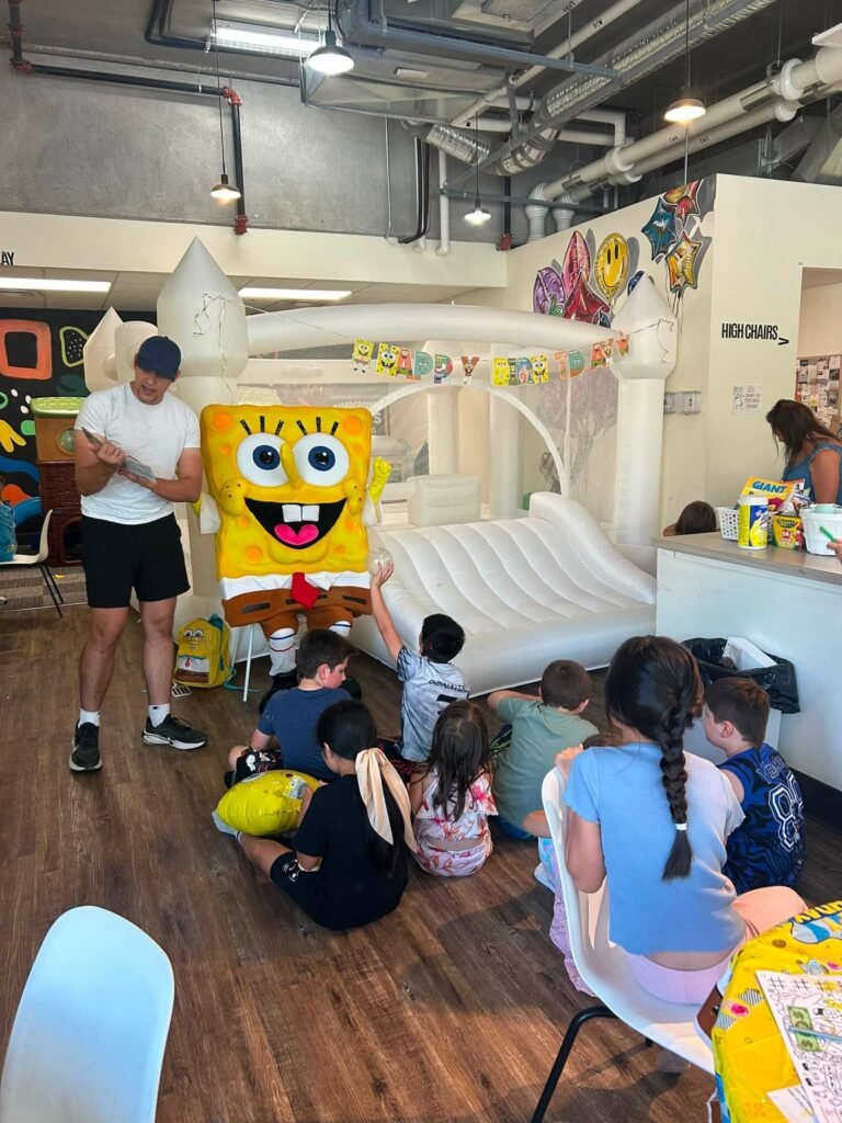 SpongeBob mascot visiting kids at an indoor party venue with a white bounce house