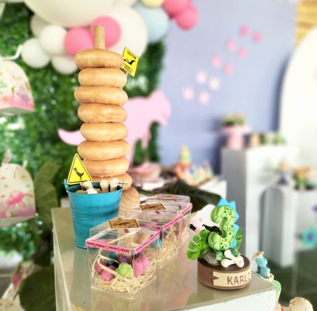 Donut tower with a dinosaur crossing sign and treat boxes on a pink dinosaur dessert table
