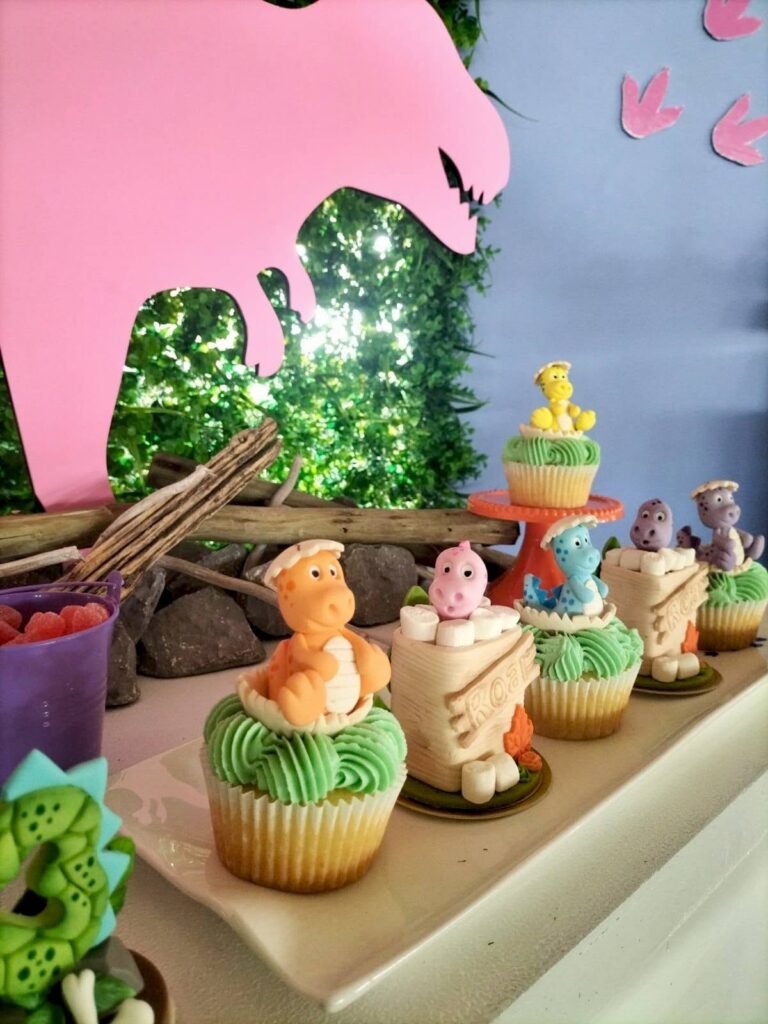 Cupcakes with baby dinosaurs and number 3 picks in front of a pink T rex cutout