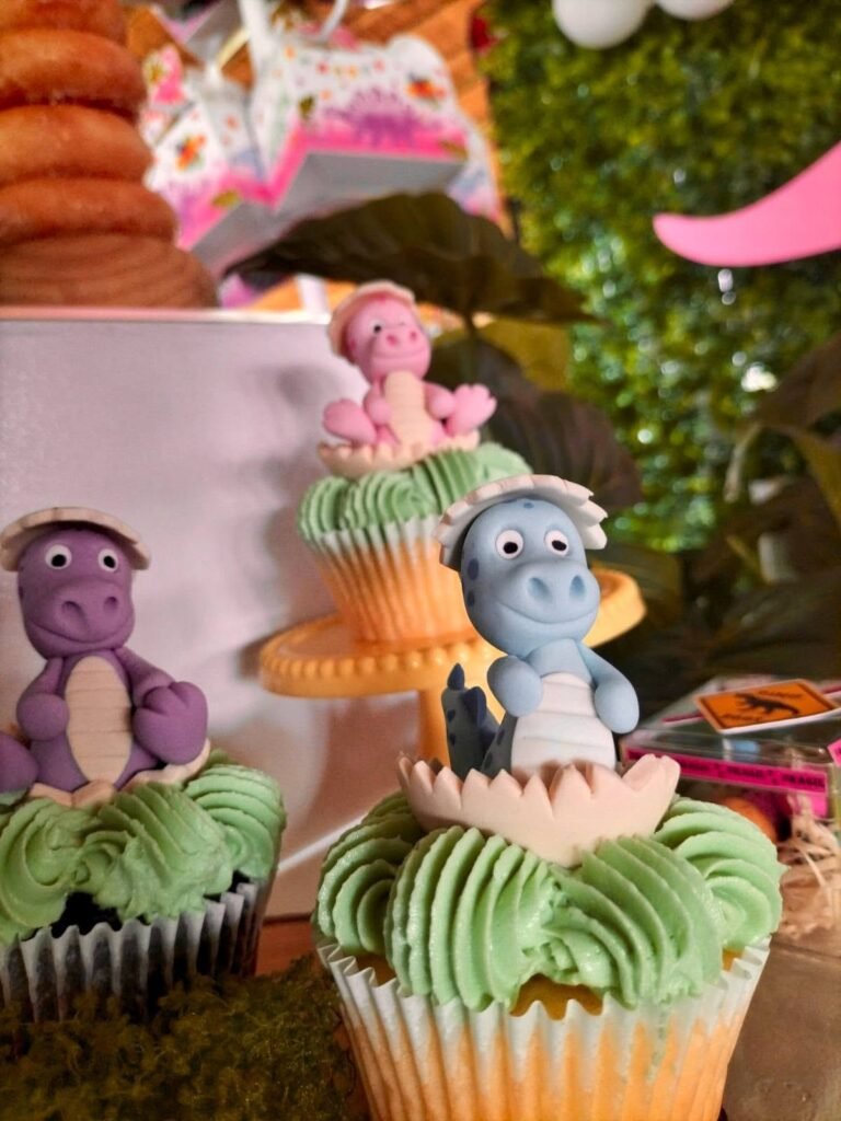 Cupcakes with purple, blue and pink baby dinosaur toppers on green frosting