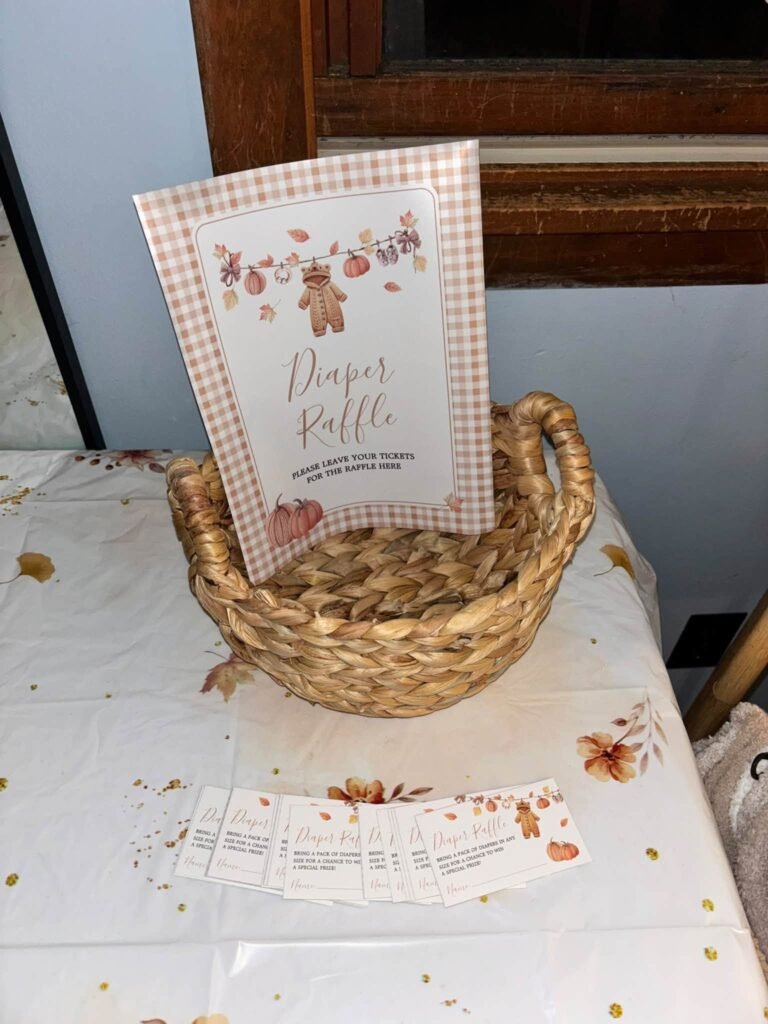 Diaper raffle sign with a fall bear in a woven basket and raffle tickets on a pumpkin print tablecloth