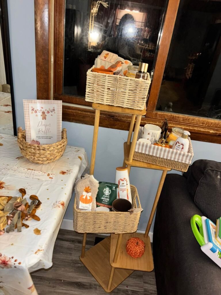 Tiered wooden stand with woven baskets of raffle prizes like coffee, candles and treats next to a diaper raffle sign