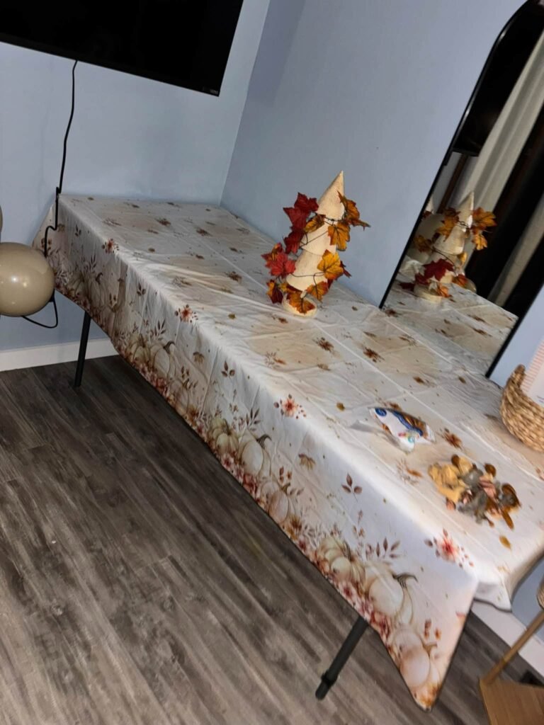 Folding table covered with a fall pumpkin print tablecloth and maple leaf centerpieces