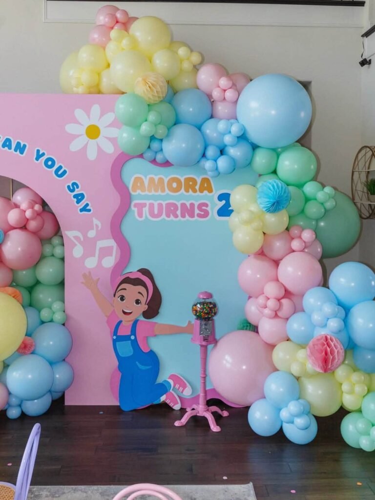 Ms Rachel 2nd birthday backdrop with a Can You Say panel, a Ms Rachel cutout, a gumball machine and a pastel balloon garland