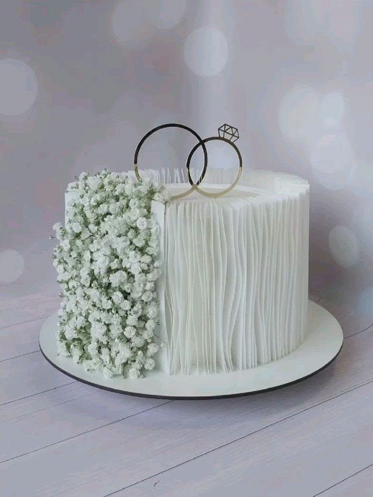 White engagement cake with half baby breath flowers and half ribbed texture and a silver ring topper