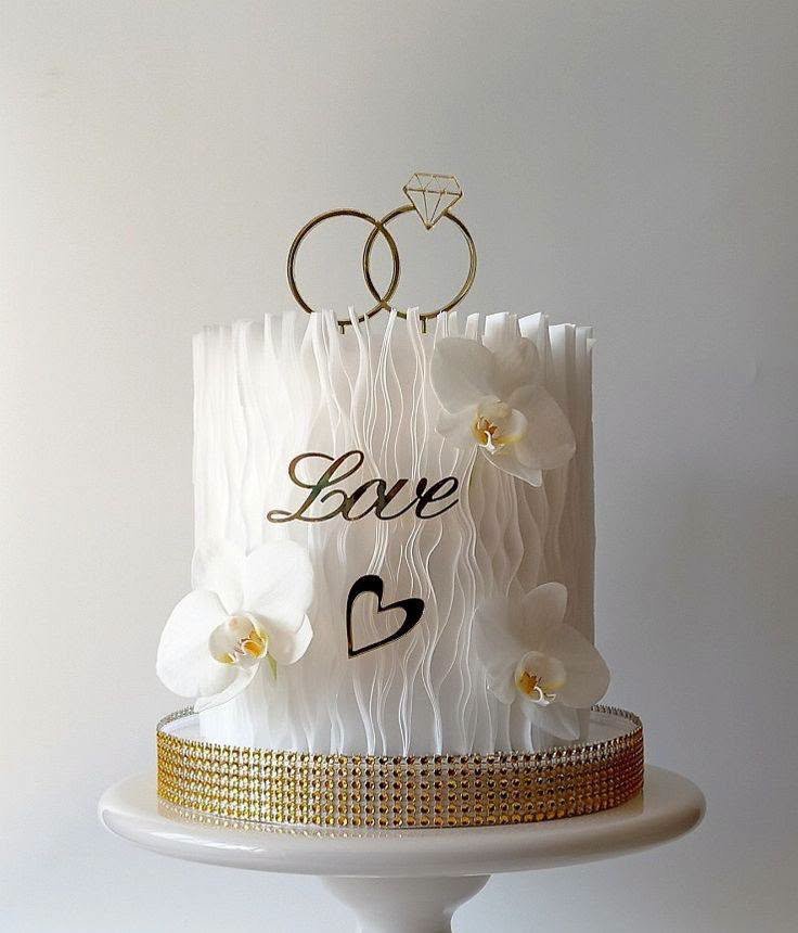 White ruffle wedding cake with white orchids, a Love script topper and gold ring topper