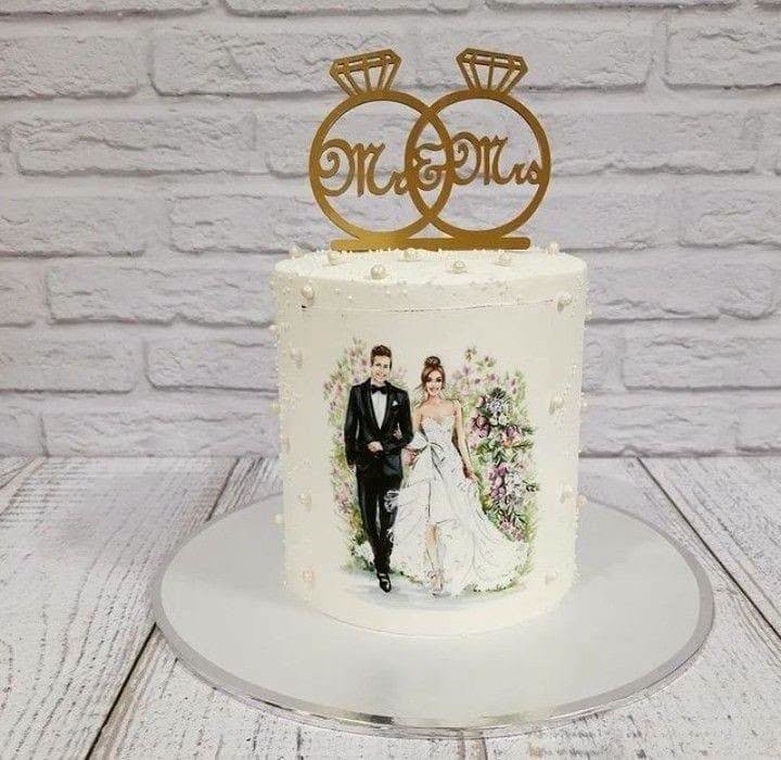 White wedding cake with a watercolor bride and groom illustration and a gold Mr and Mrs topper
